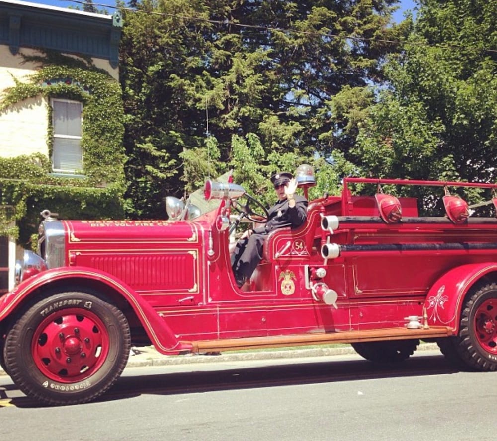 The 1936 American LaFrance fire truck out in a local parade, a firefighter waving from the driver's seat.