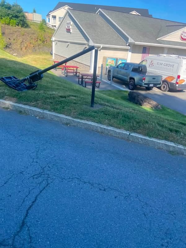 A Flock camera on a black pole snapped off and lying across the grass beside a plaza parking lot near Oakwood Avenue.
