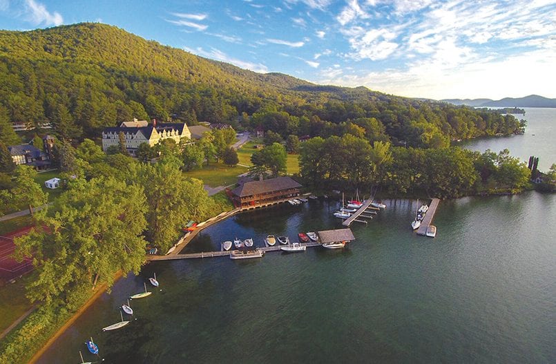 Aerial view of the Silver Bay YMCA on the wooded shore of Lake George, with historic lodge buildings, a boathouse, and docks reaching into the water.