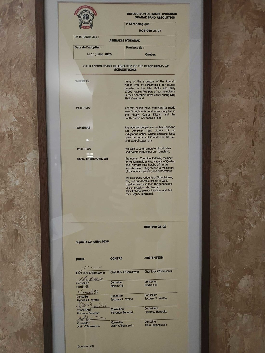 A framed two-page Odanak Band Resolution, ROB-040-26-27, adopted July 10, 2026, titled 350th Anniversary Celebration of the Peace Treaty at Schaghticoke, with four whereas clauses, a resolving clause, and the signatures of Chief Rick O'Bomsawin and four councillors, hanging on a marbled wall at Schaghticoke Town Hall.