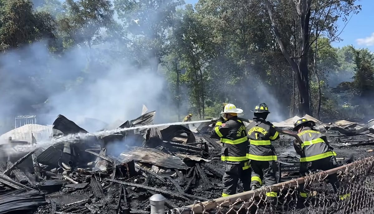 Three firefighters in Brunswick #1 turnout gear directing a hose stream onto the smoldering, blackened debris of the collapsed building.