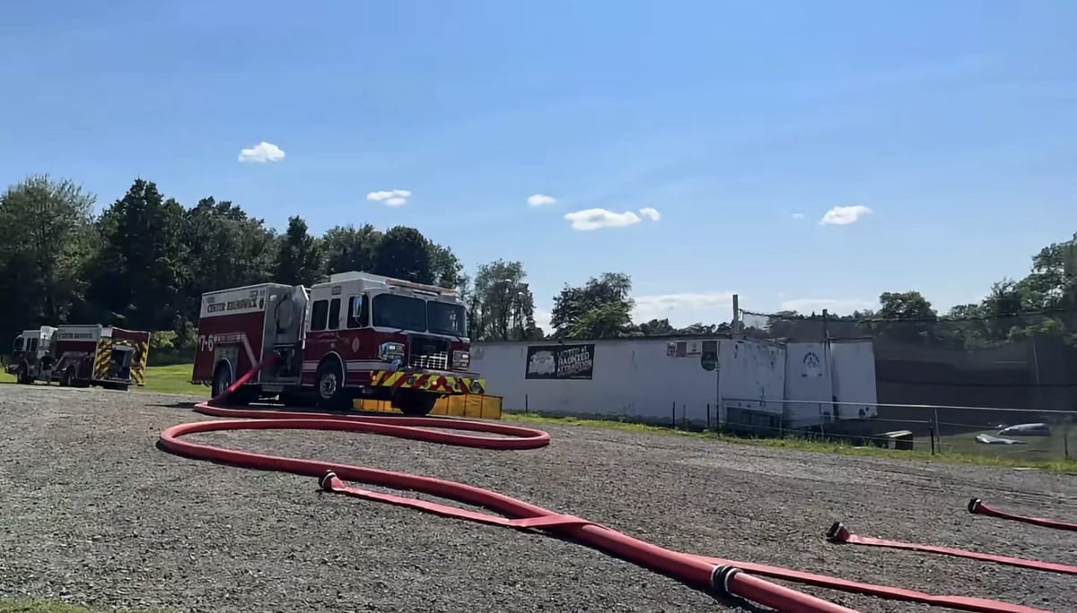 A Center Brunswick fire engine parked on gravel with supply hose laid out, beside the low white attraction building marked 'Voted #1 Haunted Attraction.'