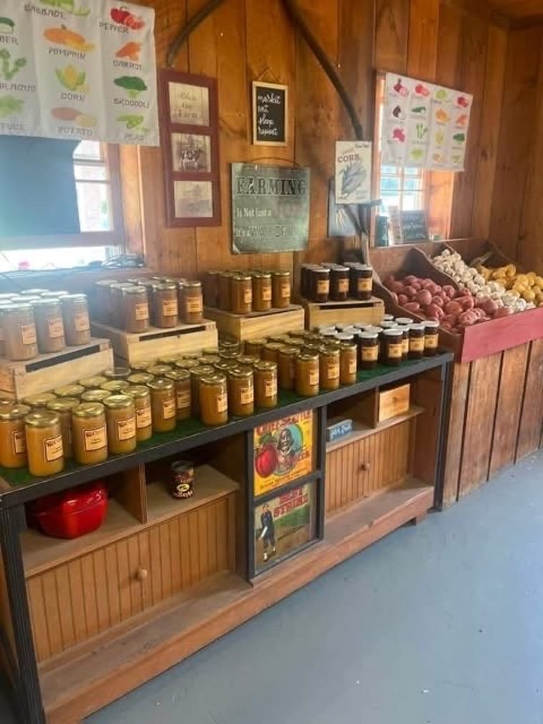 Shelves of local jams, sauces, and preserves beside bins of potatoes and garlic.