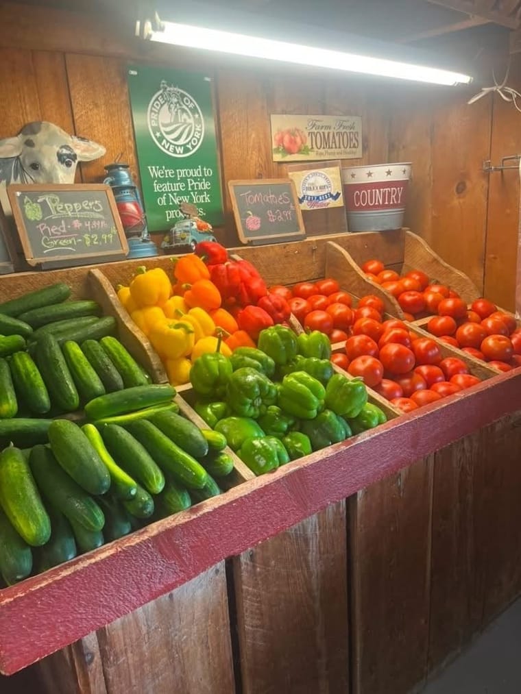 Wooden bins of cucumbers, yellow and green bell peppers, and ripe red tomatoes at Calhoun's Farm Stand.